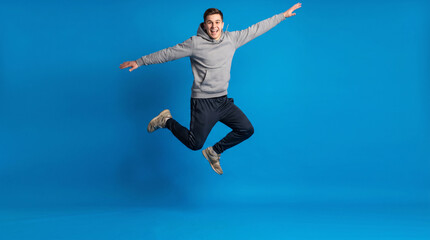 Obraz premium Young man mid jump with arms spread wide against bold electric blue background with copy space
