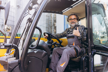 Naklejka premium Mature male worker in overalls operating an industrial vehicle, showing satisfaction and competence in his role