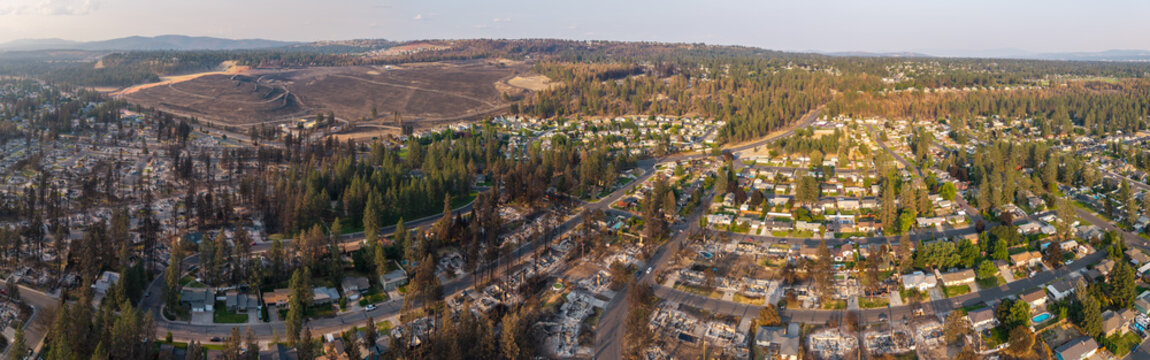 Aerial view of wildfire damage in Spokane, Washington, with charred trees and destroyed homes beside a neighboring residential area still standing.