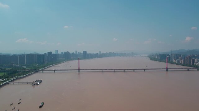 A wide muddy river crossed by a cable-stayed bridge, with urban buildings lining both banks under a clear sky.