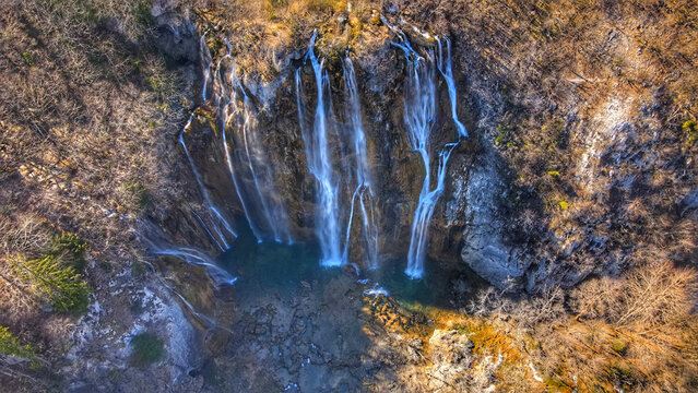 Aerial view of Plitvice Lakes National Park featuring the cascading Veliki Slap waterfall surrounded by rocky cliffs and autumn foliage in Croatia.