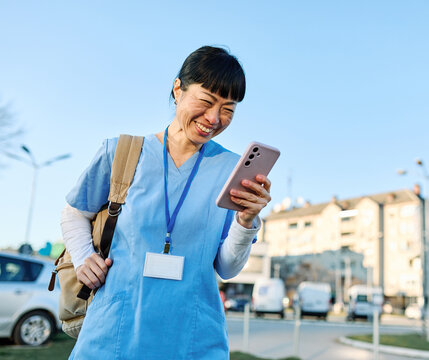 Nurse in scrubs enjoying coffee and using a mobile phone outside a modern medical facility during a sunny day