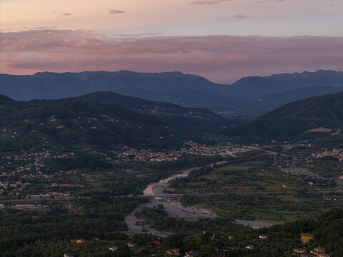Aerial view of Vezzano Ligure nestled in a lush valley with a winding river, rolling hills, and a soft sunset sky in Vezzano Ligure, Liguria, Italy.
