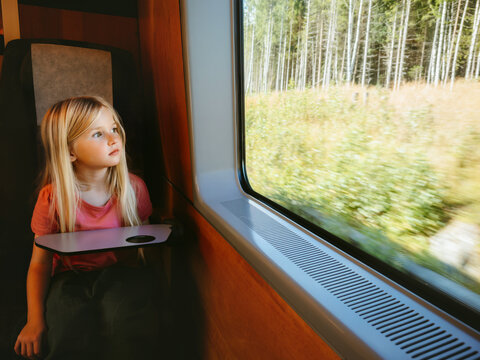 Child passenger looking out the window and thinking traveling by train with family, girl kid enjoying nature view summer vacation and railway journey by public transport sustainable travel in Europe