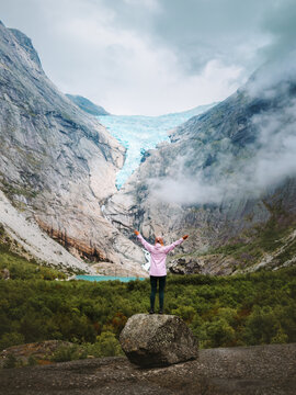 Woman solo hiker raised hands enjoying Briksdalsbreen glacier view in Norway, female traveler on active summer vacation explore Stryn discovery outdoor adventure tourism healthy lifestyle in nature