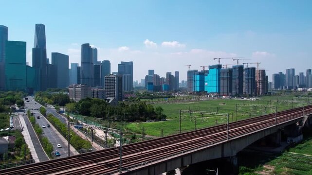 A daytime urban landscape featuring modern skyscrapers, active construction sites, and elevated railway tracks in a developing city area.