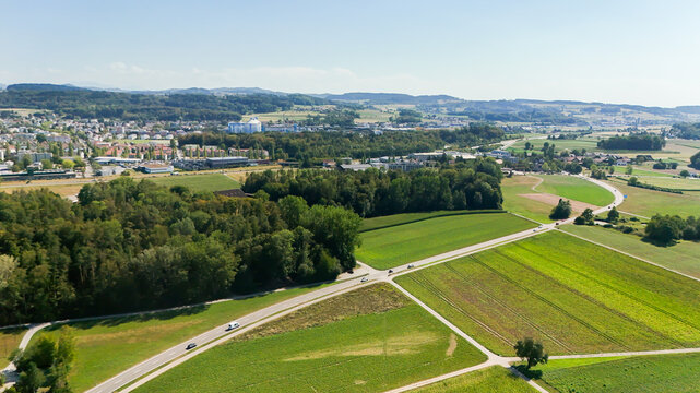 Aerial view of the town of Frauenfeld surrounded by lush green agricultural fields, winding roads, and dense forest patches in Frauenfeld, Thurgau, Switzerland.
