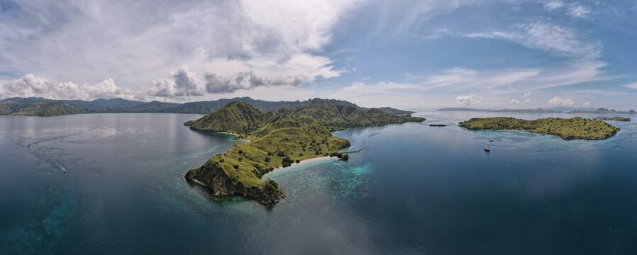 Aerial view of Komodo Island with lush green hills, turquoise waters, coral reefs, and small boats in the surrounding sea in Komodo, East Nusa Tenggara, Indonesia.