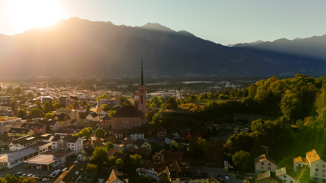 Aerial view of the town of Buchs with its prominent church spire, residential buildings, and lush greenery nestled against the backdrop of mountains in Buchs, St. Gallen, Switzerland.