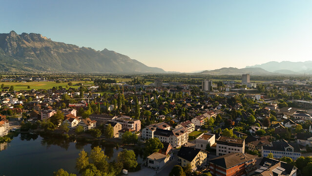 Aerial view of the town of Buchs nestled in the Rhine Valley with lush green fields and the Alps in the background under a clear sky in Buchs, St. Gallen, Switzerland.