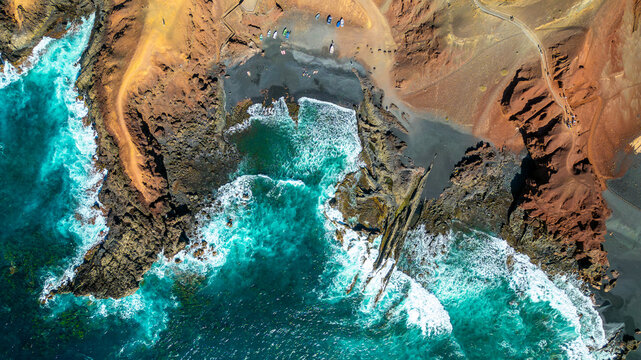 Aerial view of the volcanic coastline of Lanzarote, featuring the contrast between the black sand beach, red volcanic cliffs, and turquoise Atlantic waters in Lanzarote, Canarias, Spain.