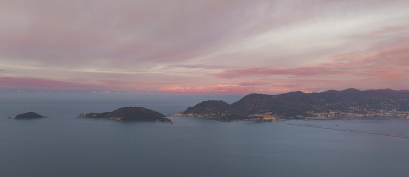 Aerial view of the coastal landscape of Tellaro at sunset with soft pink clouds over the sea and rolling hills in Tellaro, Liguria, Italy.