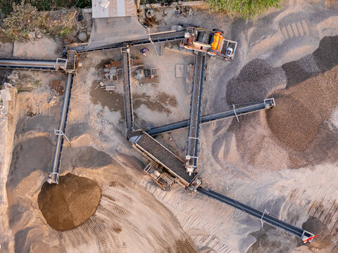 Aerial view of a stone crushing plant with conveyor belts transporting gravel and sand piles in an industrial quarry in Manisrenggo, Central Java, Indonesia.