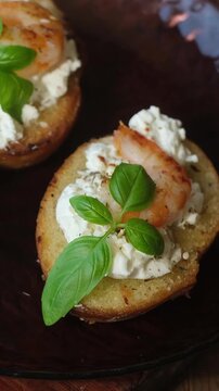  Vertical video.Bruschetta or crostini topped with cream cheese, shrimp and fresh basil. Tasty healthy snacks on wooden board.