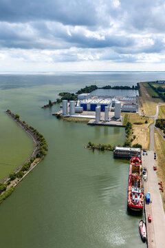 Aerial view of an industrial site with storage tanks, silos, and windmill components ready for installation, located along a canal in Wieringerwerf, North Holland, Netherlands.