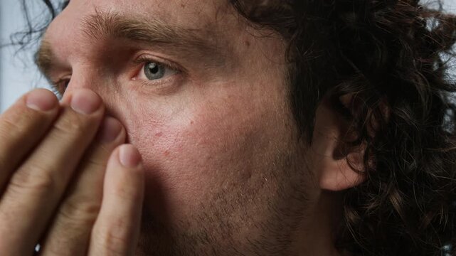 Young Caucasian man applying moisturizing cream on face, extreme close up. Footage is ideal for male grooming products, skincare advertisements, and dermatology clinic promotions