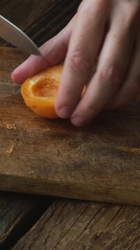 Vertical video. Hands cutting fresh apricots with a knife. Summer seasonal fruits.