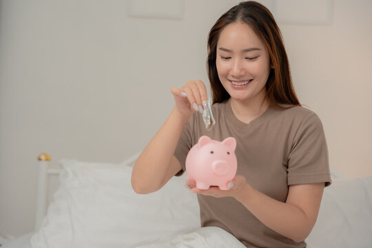 Saving money, financial planning and future goals concept. Happy young Asian woman holds a pink piggy bank at home. Savings, finance, investment, budget, future