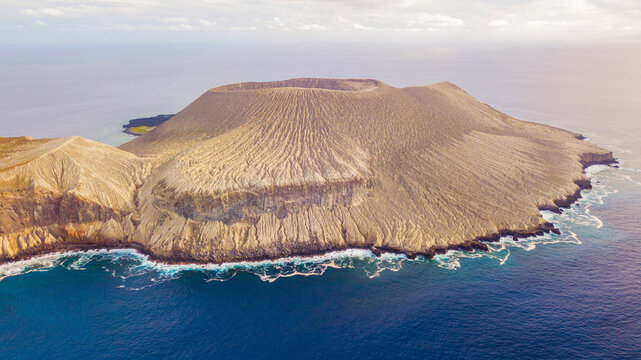 Aerial view of San Benedicto Island with its prominent volcanic crater, rugged slopes, and rocky coastline surrounded by the deep blue Pacific Ocean in Colima, Mexico.