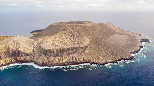 Aerial view of San Benedicto Island, a volcanic island with rugged terrain and dramatic crater, surrounded by the deep blue Pacific Ocean in Colima, Mexico.