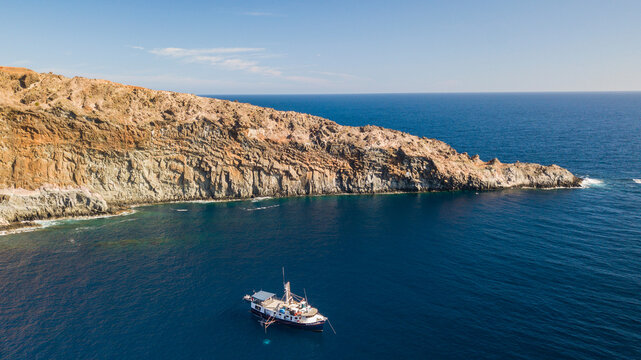 Aerial view of a boat anchored near the rugged volcanic cliffs of Socorro Island, Colima, Mexico.
