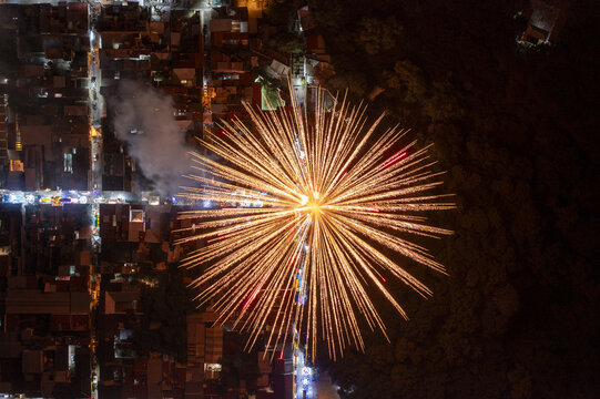 Aerial view of fireworks display over the Barrio de Santiago party with bright golden light trails illuminating the night sky above the urban streets Uruapan, Michoacan, Mexico.