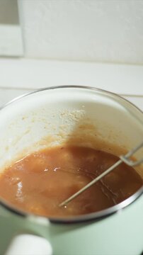 Close up of brown liquid thickening in pot with metal utensil. Sauce simmers and becomes more viscous. Utensil remains partially submerged throughout sequence with brown