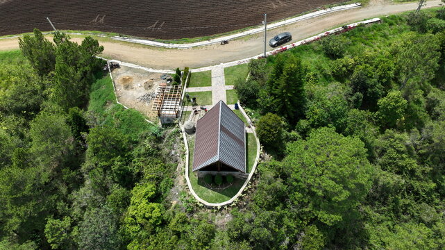 Aerial view of the Portezuelo landmark surrounded by lush green trees, a dirt road, and agricultural fields in Constanza, La Vega, Dominican Republic.