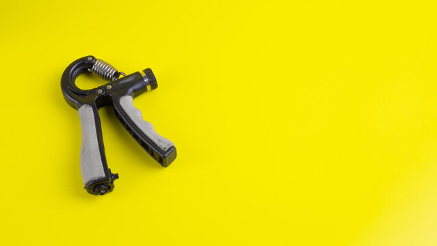 Flat lay adjustable hand gripper on bright yellow background with ample copy space. Ideal fitness tool for grip strength and muscle rehabilitation.
