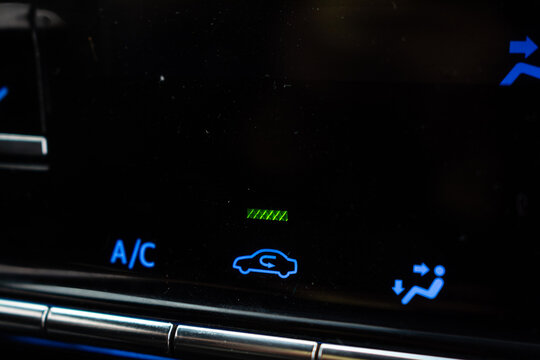 Close-up of car air conditioner control panel with blue illuminated A/C and air recirculation symbols
