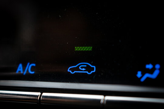 Close-up of car air conditioner control panel with blue illuminated A/C and air recirculation symbols
