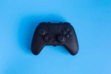 Black wireless gamepad controller isolated on solid blue background. Minimalist flat lay concept for gaming and esports advertising.  © wibiwisnu