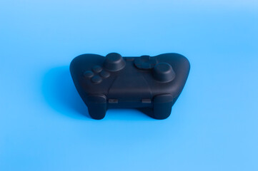 Angled view of black wireless gamepad controller on solid blue background. Minimalist design for esports, gaming mockup, and tech advertising.  © wibiwisnu