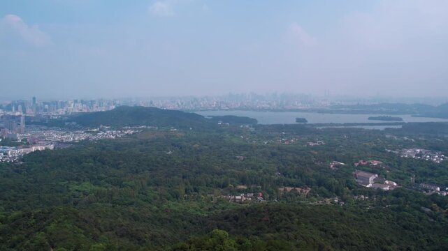 A wide-angle panorama shows a green hilly landscape with a lake, distant urban buildings under a clear sky.