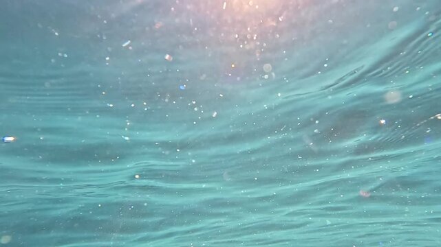 Sunlit tropical water ripples illuminate the deep ocean floor. Underwater low-angle shot displays shimmering light beams refracting through the clear moving surface.