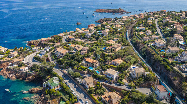 Aerial view of a passenger train traveling along the Mediterranean coast, winding through a residential area with villas and rocky coves Saint-Raphael, Provence-Alpes-Cote d'Azur, France.
