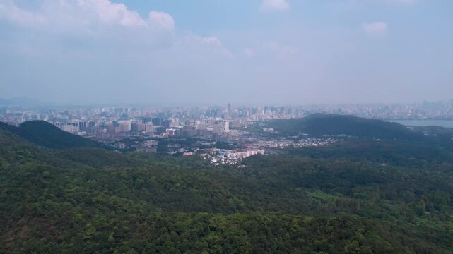A panoramic view shows dense forest in the foreground with an urban area stretching under a clear sky in the distance.