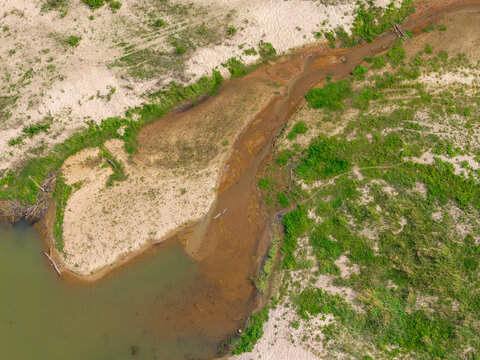 Aerial view of sandbanks and low water levels in a riverbed during a heat wave, surrounded by green vegetation and dry sandy banks in Poland.
