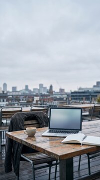 Hazy city skyline behind a rooftop cafe table with a laptop template and coffee