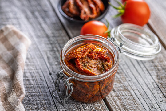 Jar of Sun-Dried Tomatoes in Olive Oil on Rustic Wooden Table with Fresh Tomatoes