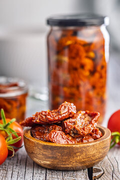 Sun-Dried Tomatoes in Olive Oil in Wooden Bowl with Jars on Rustic Table