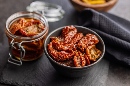 Sun-Dried Tomatoes in Olive Oil Jar and Bowl on Dark Slate for Gourmet Mediterranean Cooking