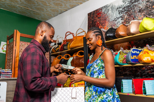African female entrepreneur receiving cash payment from male customer for a shopping purchase in her handbag store