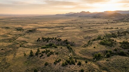 Fototapeta premium Panoramic Aerial View of Expansive Rolling Hills and Winding River Valley with Distant Mountains at Golden Sunset