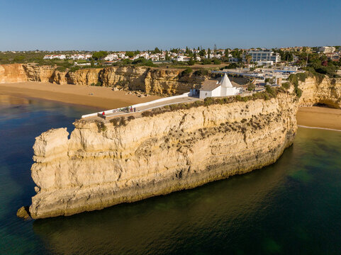 Aerial view of the Chapel of Nossa Senhora da Rocha perched on a rocky cliff overlooking the Atlantic Ocean and sandy beaches in Faro District, Portugal.