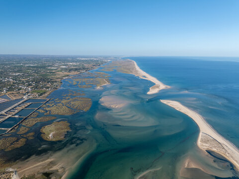 Aerial view of the Ria Formosa coastal lagoon with its intricate tidal channels, sandbanks, and salt pans stretching along the coastline of Faro District, Portugal.