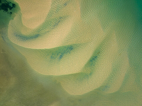 Aerial view of intricate sandbars and tidal patterns in shallow turquoise water along the coast, Faro District, Portugal.