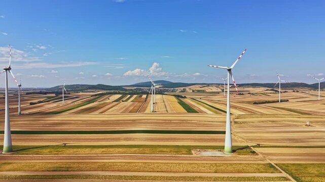 Wind turbines are turning in the field while rows of crops stretch out below. The sky is clear with some clouds in the distance. This scene shows a modern energy source.