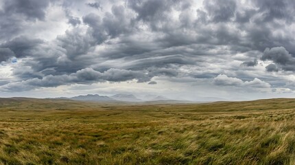 Fototapeta premium Dramatic Stormy Sky Over Vast Grassy Moorland Landscape with Distant Mountain Peaks and Moody Overcast Atmosphere
