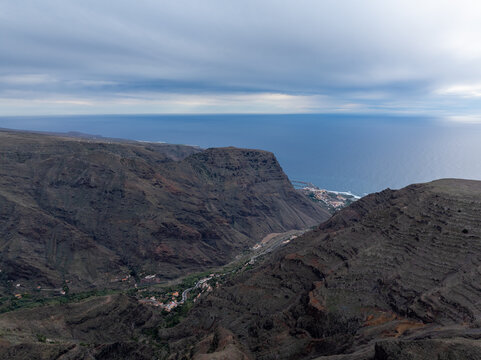 Aerial view of the rugged volcanic landscape of La Palma with deep ravines, coastal cliffs, and a small settlement nestled in the valley in the Canary Islands, Spain.